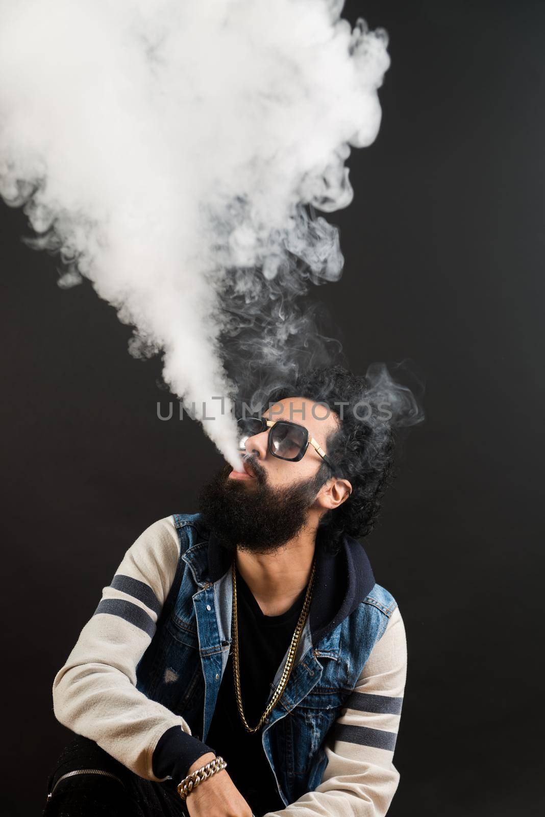 Young man with beard vaping an electronic cigarette upwards. Vaper hipster smoke vaporizer. Black background