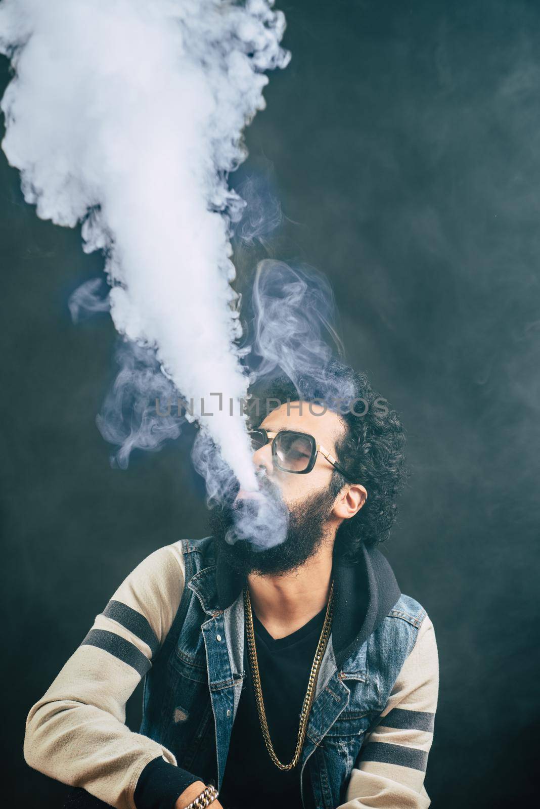 Young man with beard vaping an electronic cigarette upwards. Vaper hipster smoke vaporizer. Black background