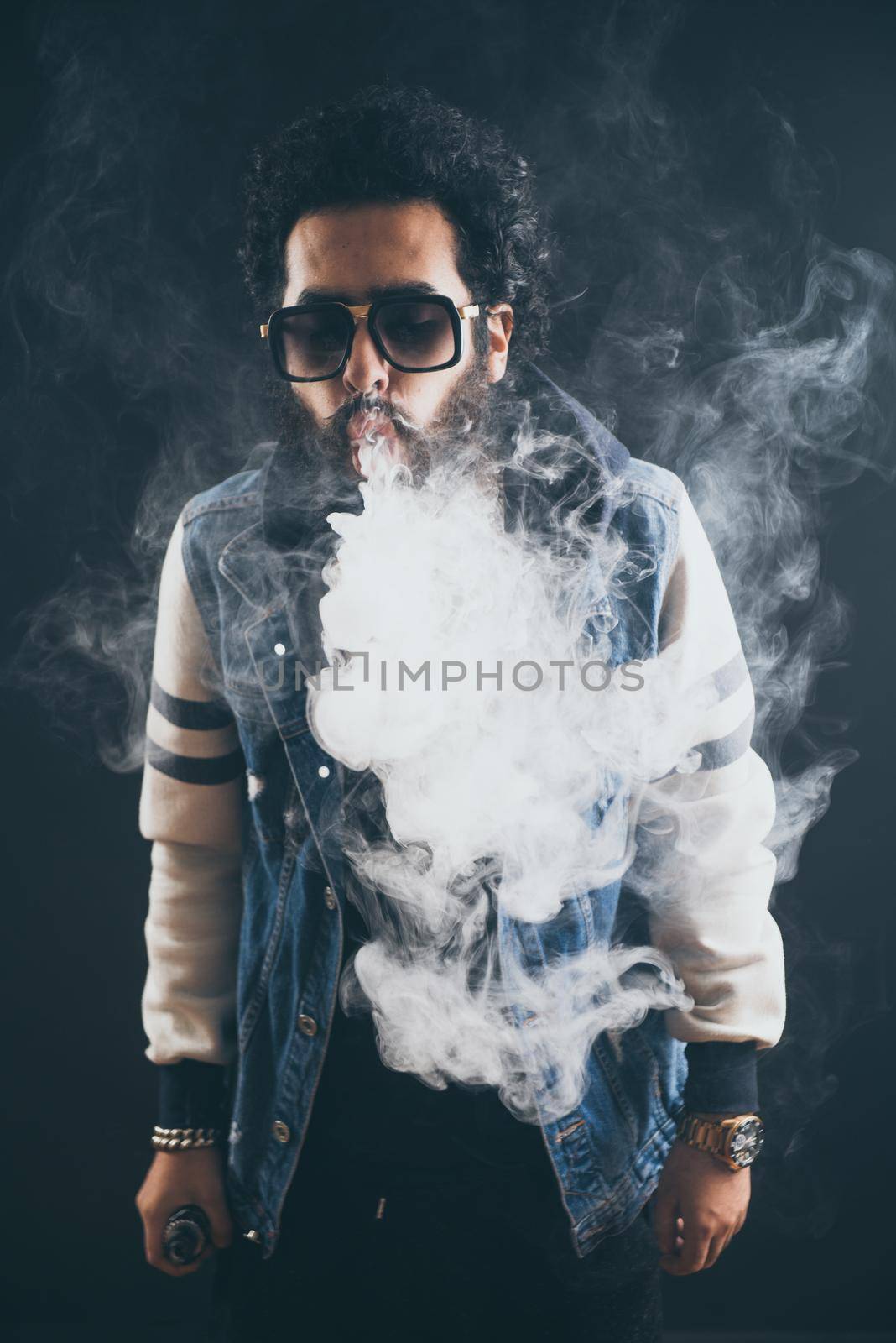 Vaping man holding a mod. A cloud of vapor. Black background. Vaping an electronic cigarette with a lot of smoke. Vape concept