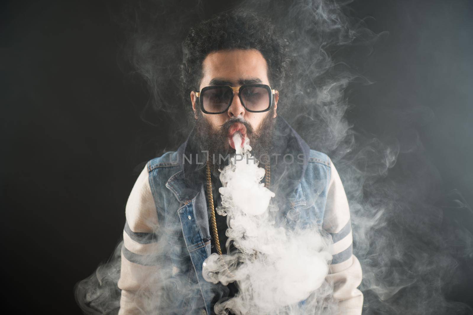 Vaping man holding a mod. A cloud of vapor. Black background. Vaping an electronic cigarette with a lot of smoke. Vape concept