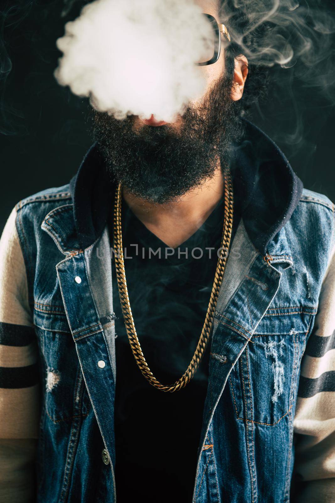 Young man with beard throwing a cloud of steam. Black background. Vaping an electronic cigarette with a lot of smoke