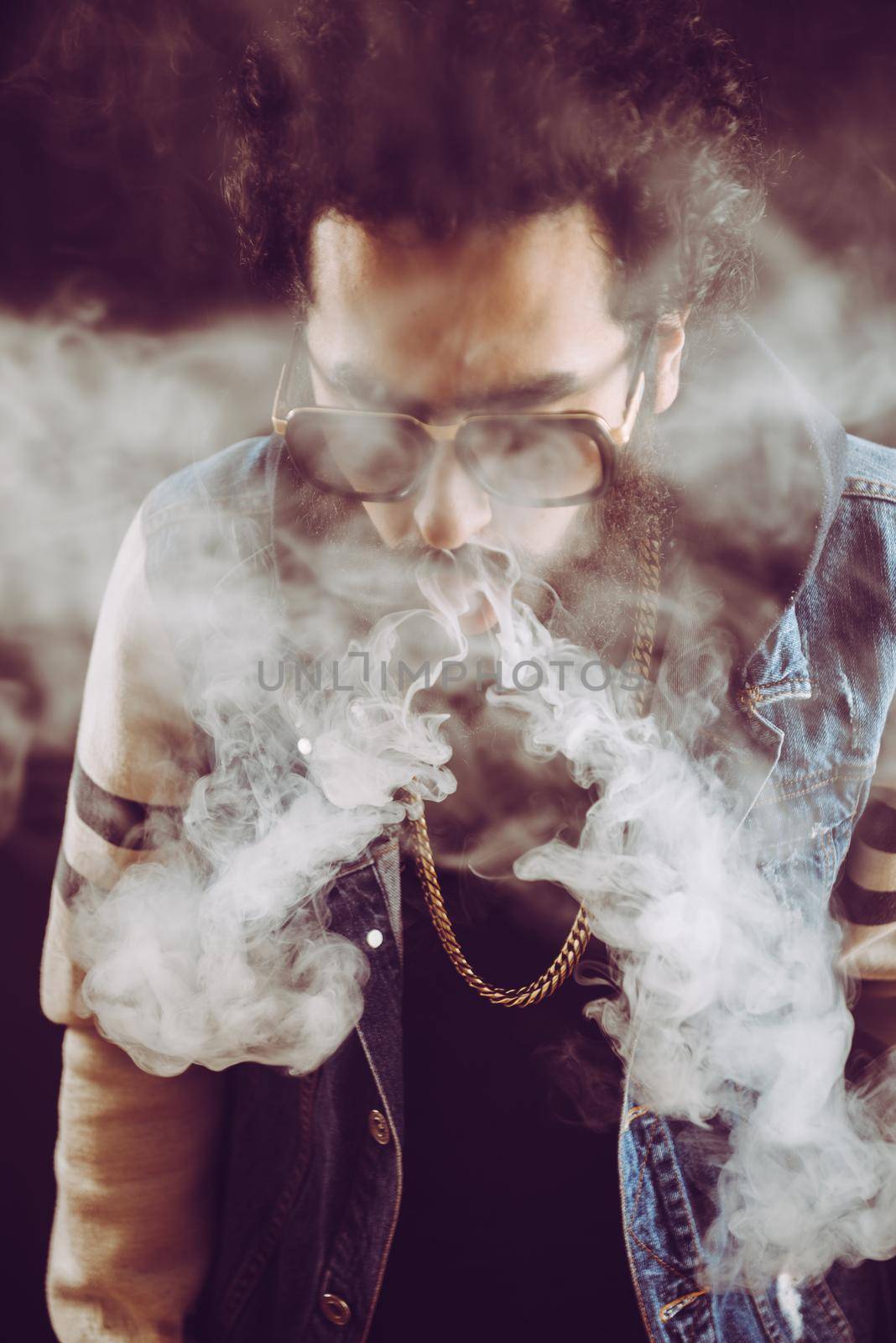 Young man with beard throwing a cloud of steam. Black background. Vaping an electronic cigarette with a lot of smoke