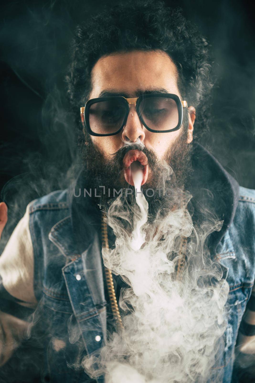 Young man with beard throwing a cloud of steam. Black background. Vaping an electronic cigarette with a lot of smoke