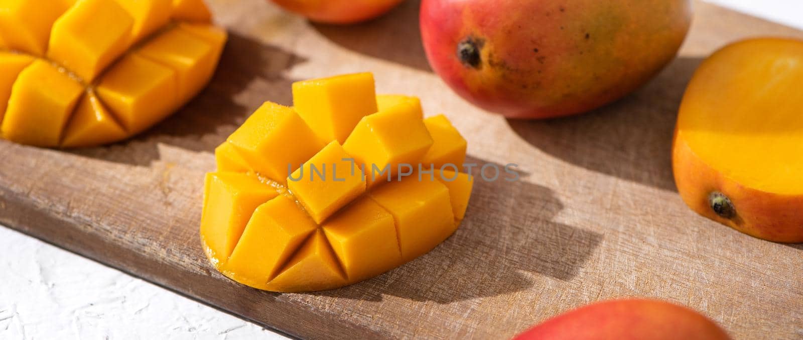 Diced fresh mango fruit on wooden cutting board with sunlight and leaf shadow at home kitchen in the afternoon.
