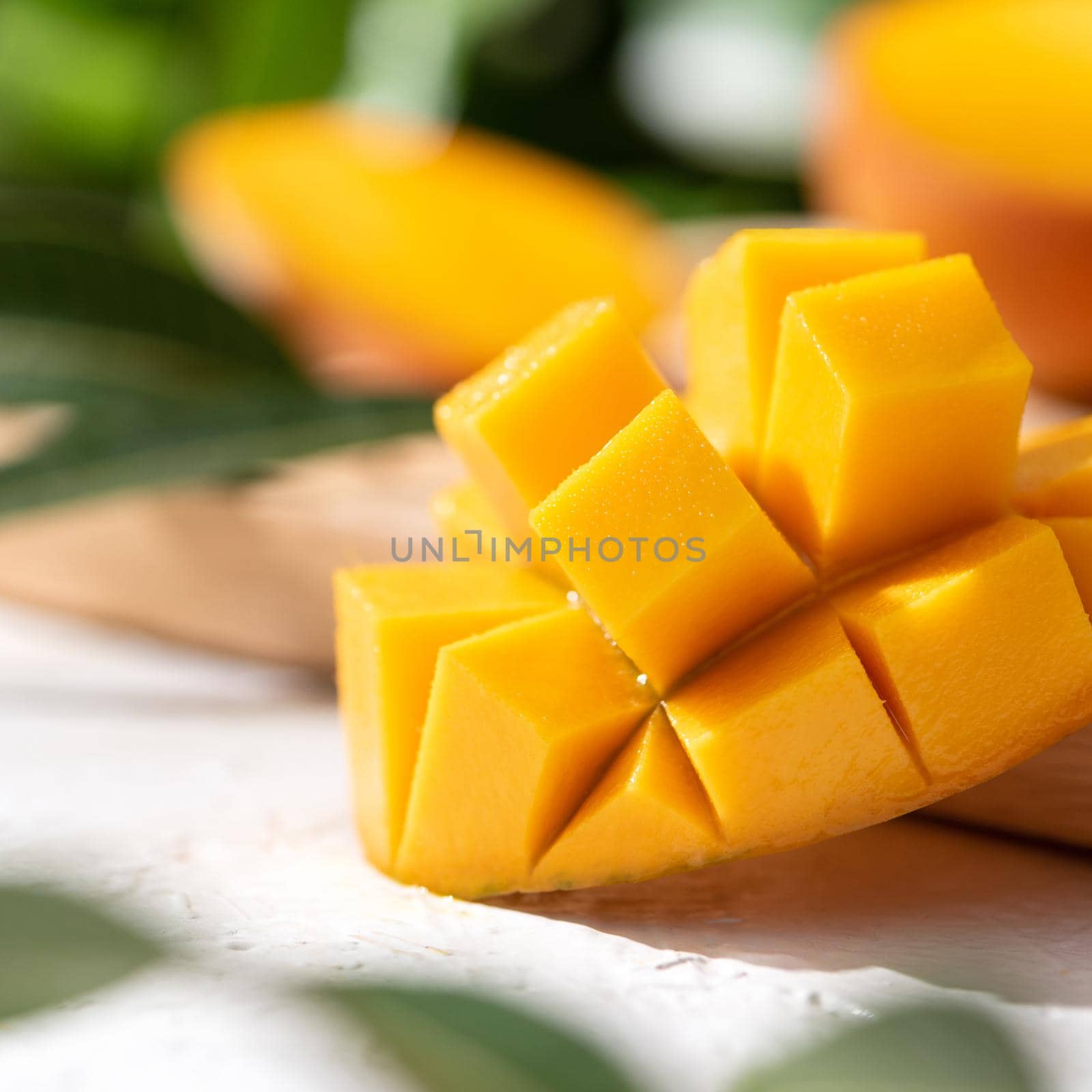 Diced fresh mango fruit on wooden cutting board with sunlight and leaf shadow at home kitchen in the afternoon.