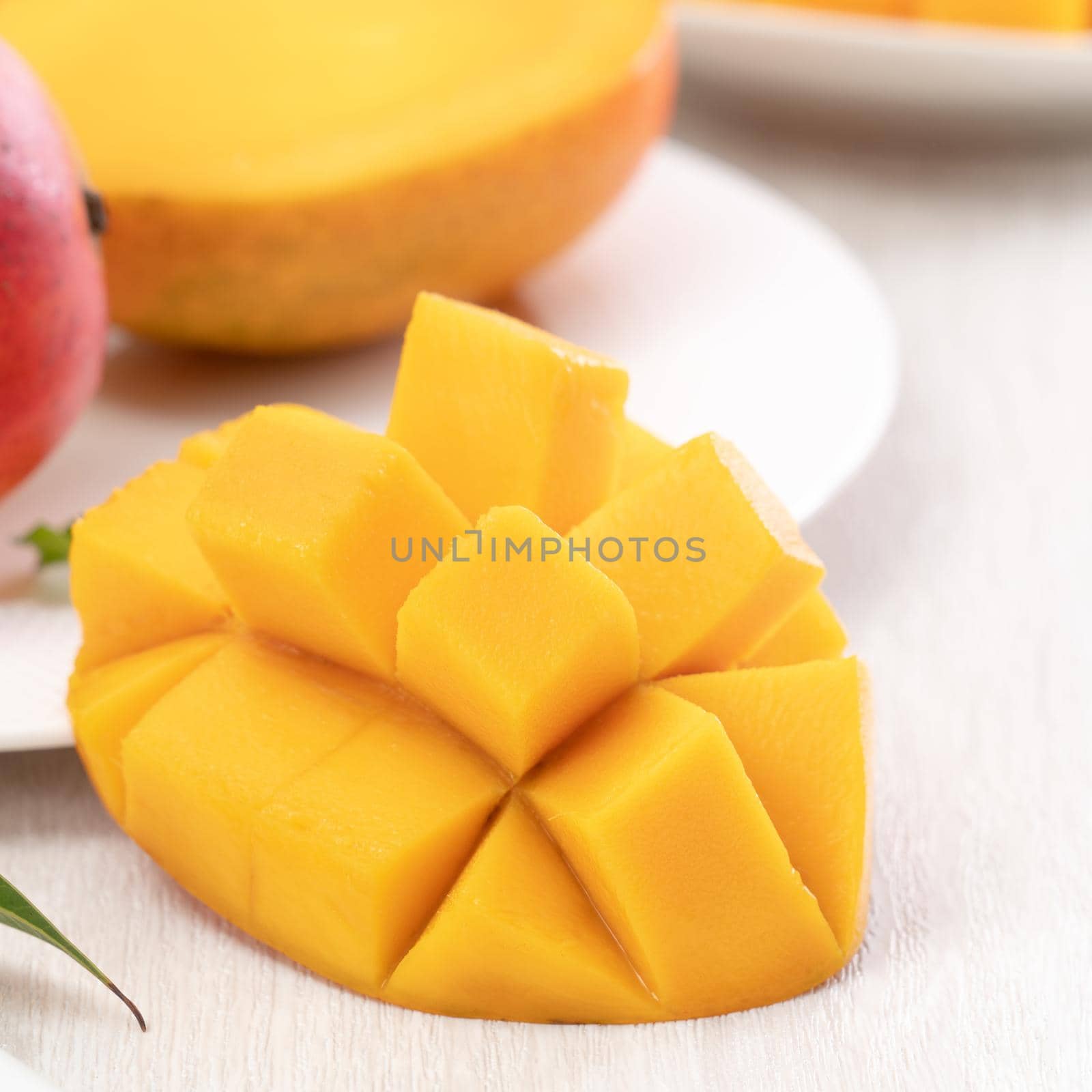 Diced fresh mango fruit on a white plate with leaves over wooden table background.