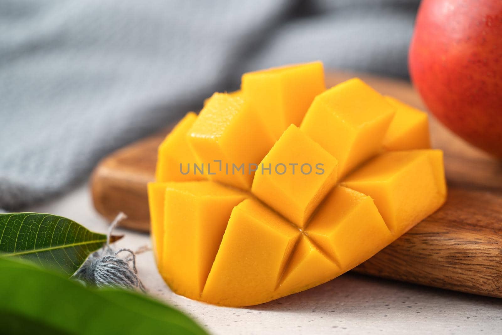 Diced fresh mango fruit on a white plate over wooden cutting board with leaves on gray table background.