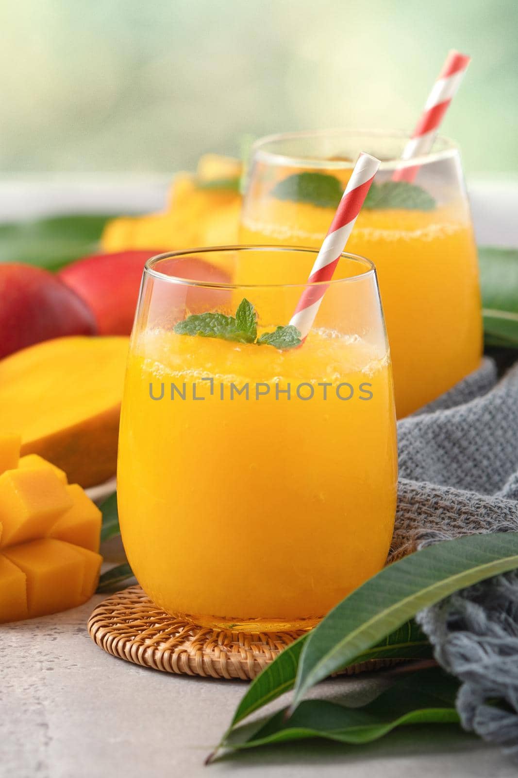 Fresh beautiful delicious mango juice. Close up design concept of smoothie cold drink in a glass cup with paper straw on gray table background.