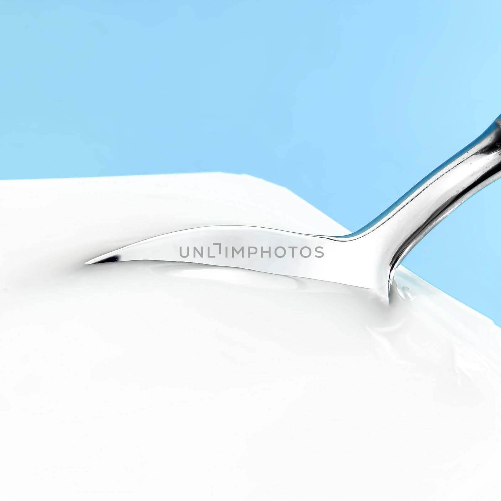 Yogurt cup and silver spoon on blue background, white plastic container, fresh dairy product for healthy diet and nutrition.