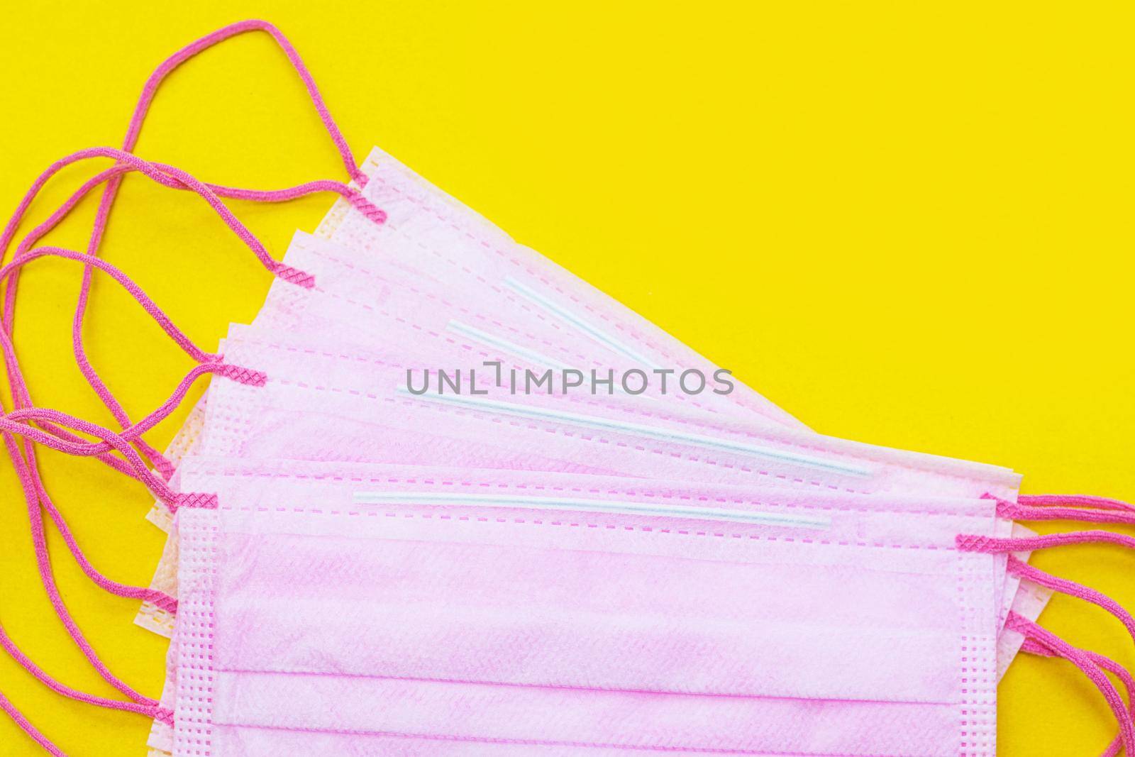 Medical mask isolated on a yellow background . Pink face mask. Article about the second wave of coronavirus. Protection of the respiratory system. Pneumonia and coronavirus. Pandemic. Copy space