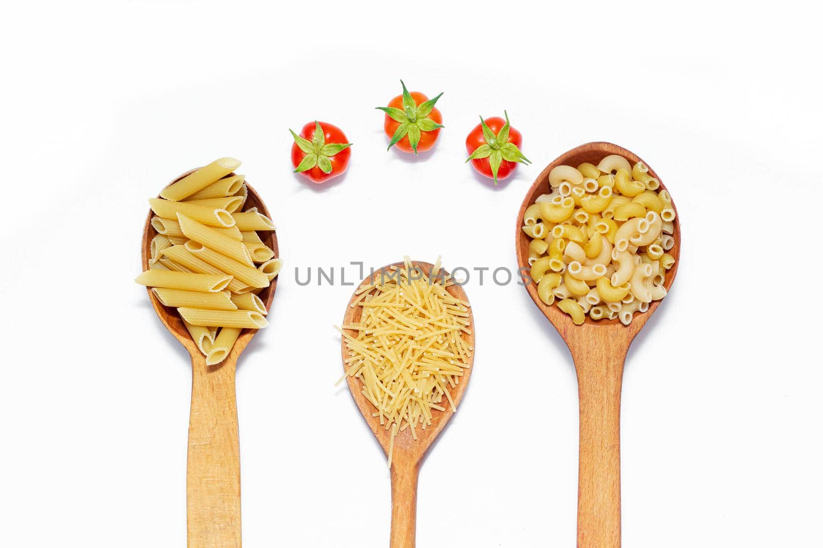 Macaroni several types in wooden spoons on a white background . Macaroni on wooden spoons . Macaroni on a white background. Article about the choice of pasta. Ingredients for the dish. Copy space . Isolated background. Food supply . Cherry tomatoes. Cooking pasta