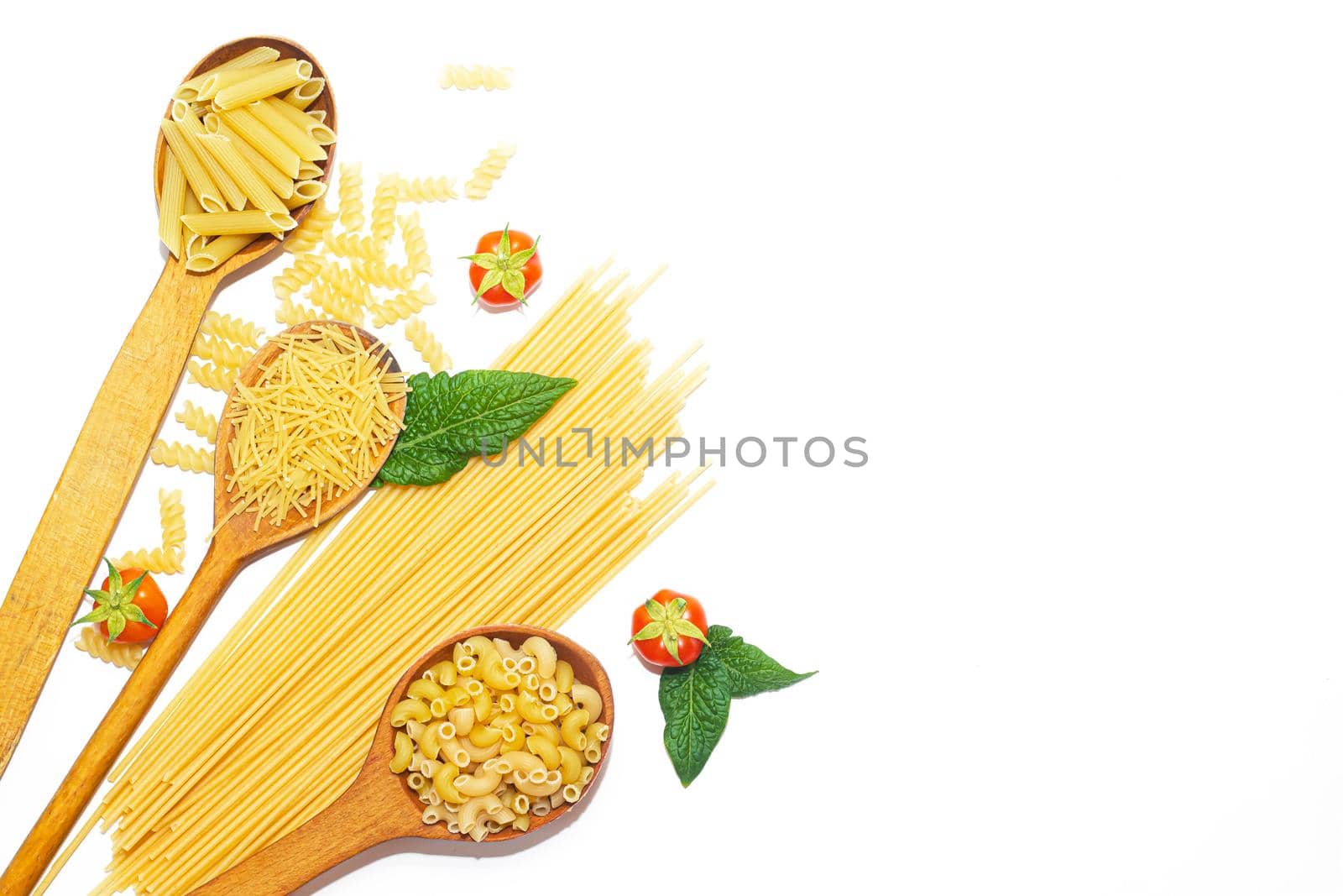 Macaroni several types in wooden spoons on a white background . Macaroni on wooden spoons . Macaroni on a white background. Article about the choice of pasta. Ingredients for the dish. Copy space . Isolated background. Food supply . Cherry tomatoes. Cooking pasta