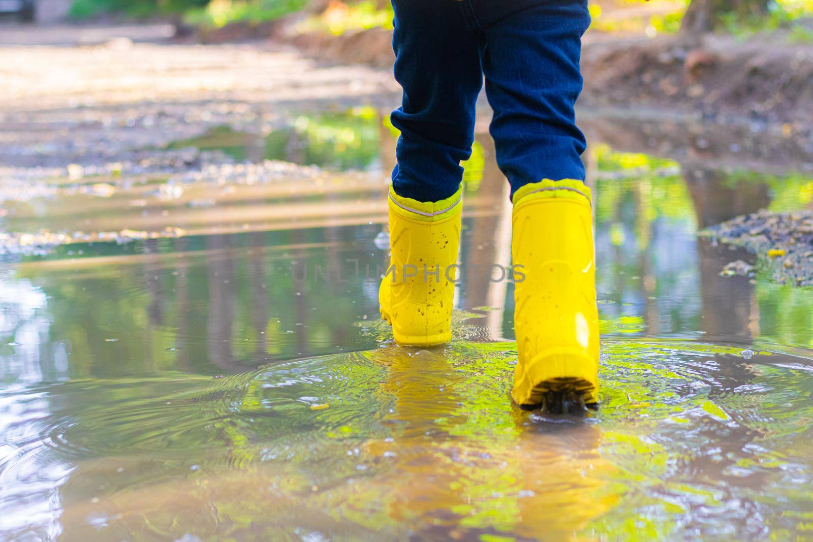 the boy jumps in a puddle. a boy in rubber boots. summer fun. game in town. children's entertainment. the article is about the holiday in the city . by alenka2194