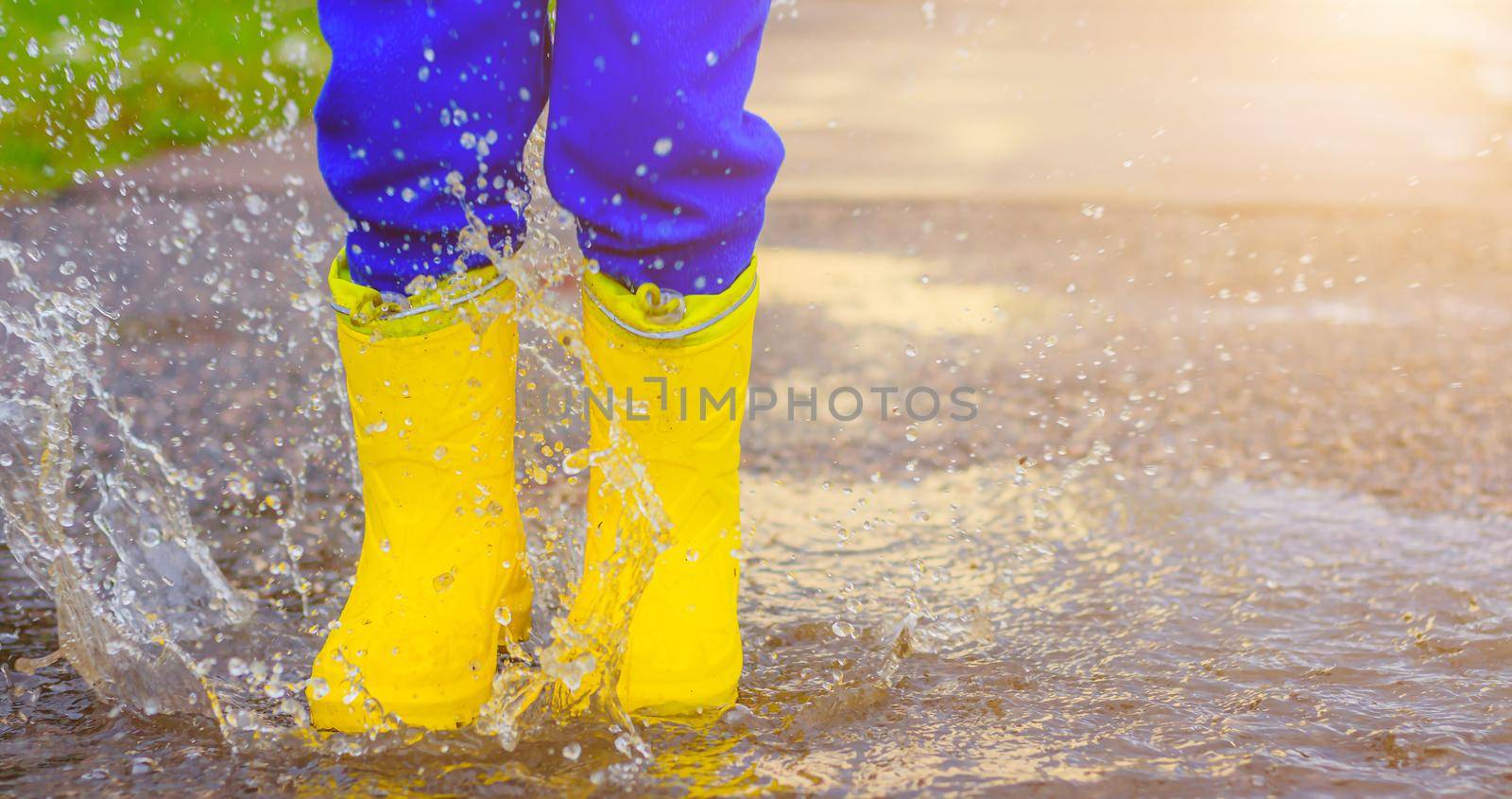 My rubber-booted feet are Bouncing in a puddle. Article about rubber boots. Children's summer shoes. Puddles after rain. Bad weather. A child jumps in a puddle. A happy boy in rubber boots jumps in puddles.