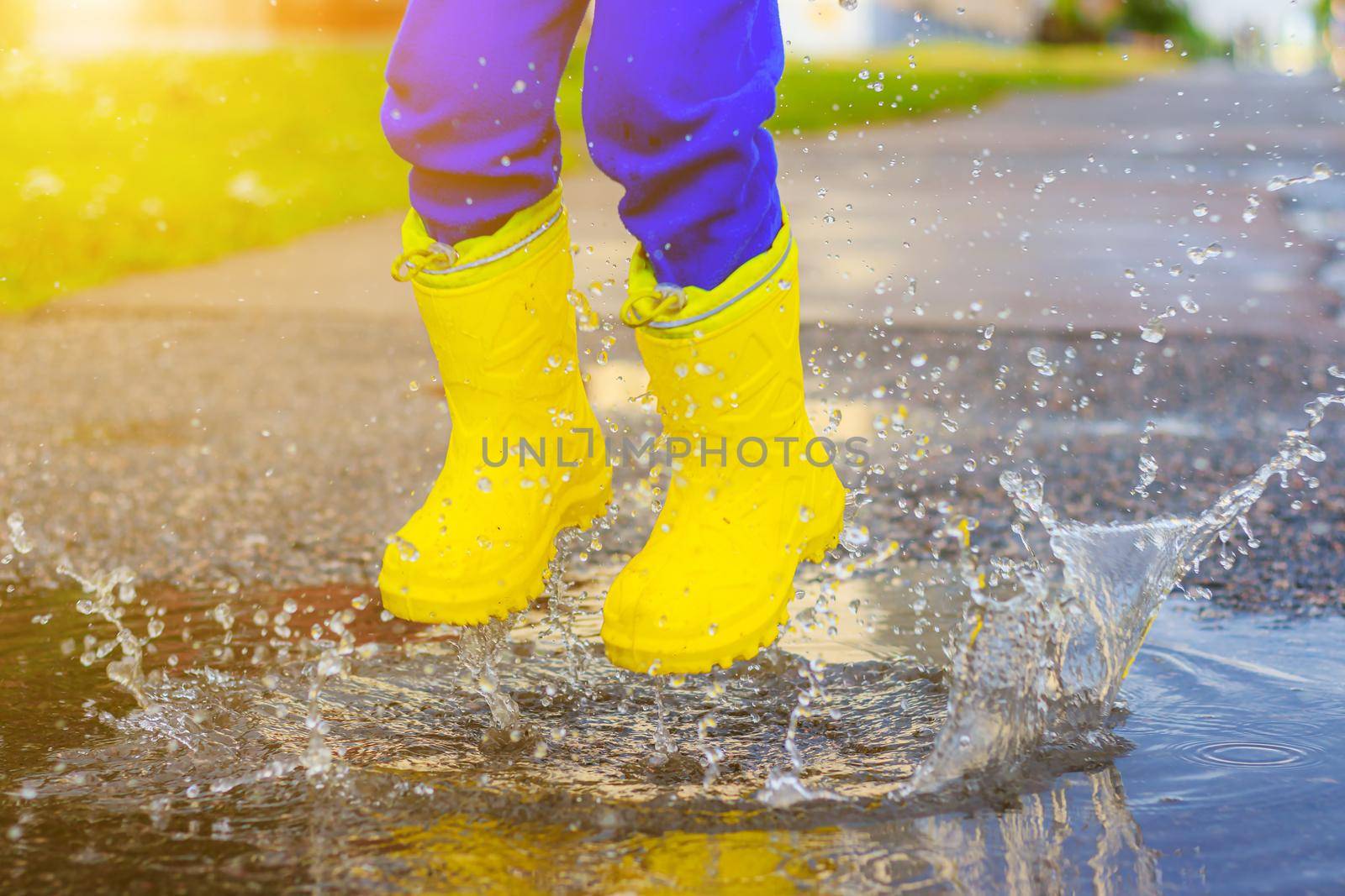 My rubber-booted feet are Bouncing in a puddle. Article about rubber boots. Children's summer shoes. Puddles after rain. Bad weather. A child jumps in a puddle. A happy boy in rubber boots jumps in puddles.