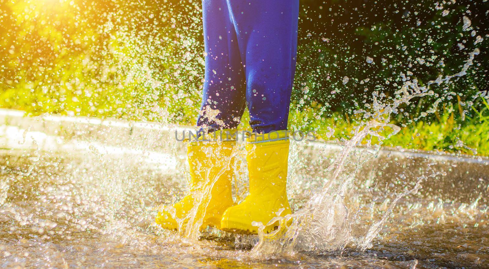 My rubber-booted feet are Bouncing in a puddle. Article about rubber boots. Children's summer shoes. Puddles after rain. Bad weather. A child jumps in a puddle. A happy boy in rubber boots jumps in puddles.