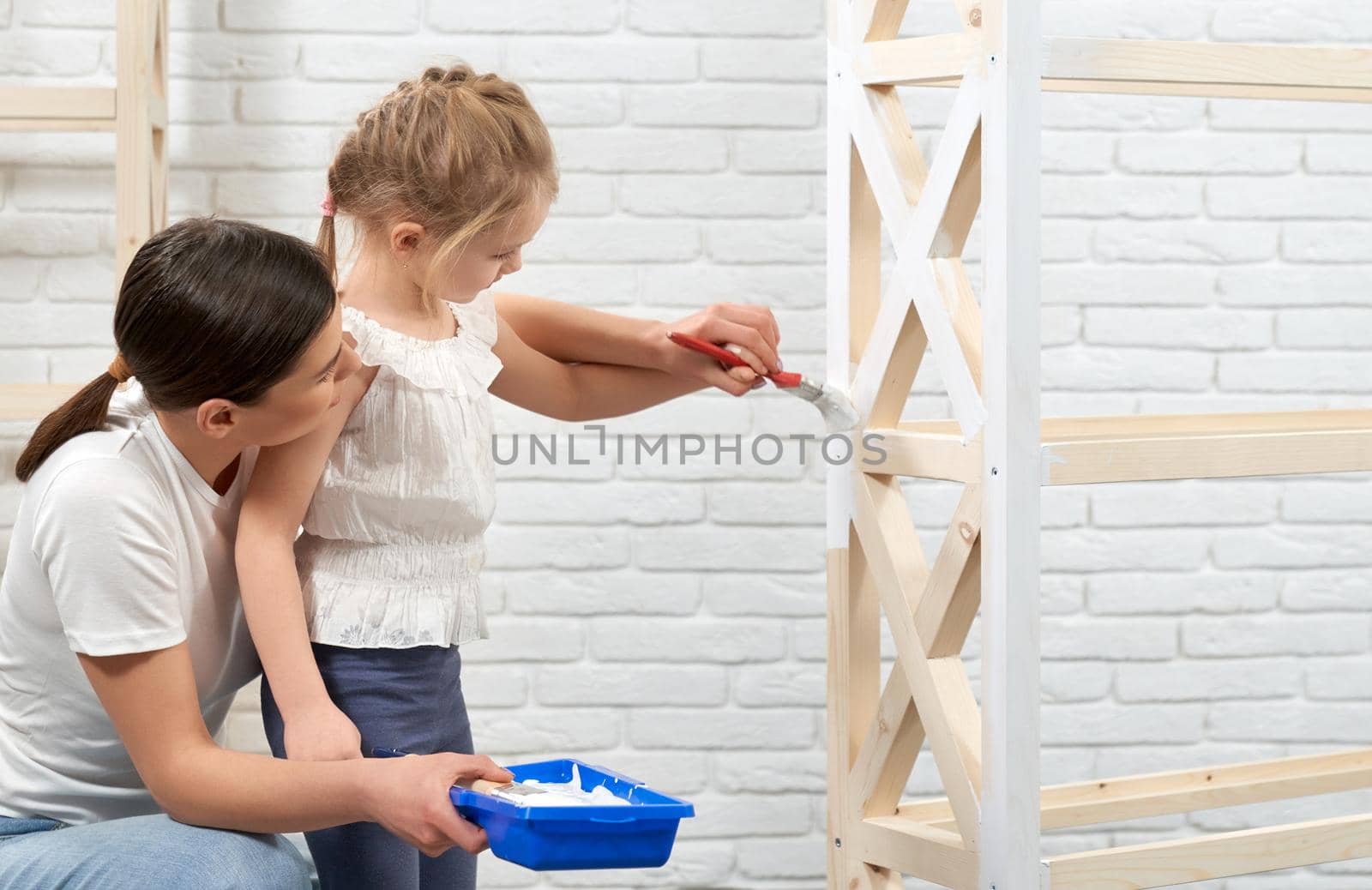 Close up of young mother and child painting wooden rack at home. Concept of family time.