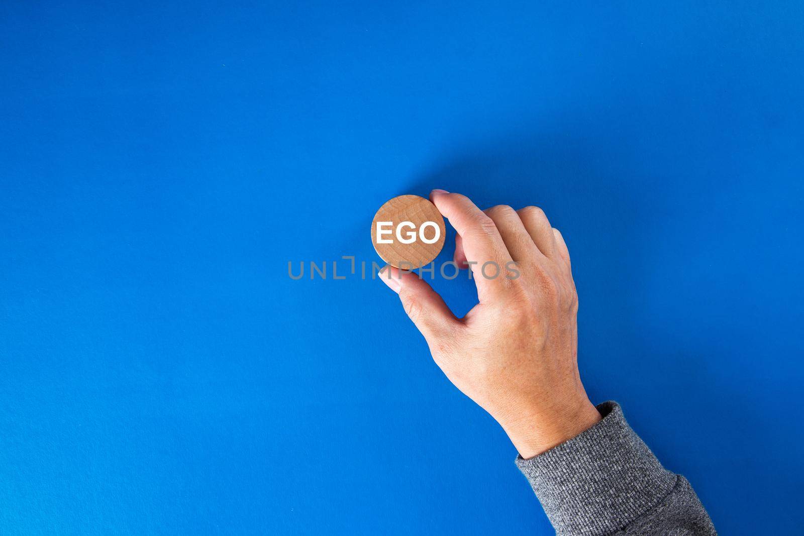 Businessman hand holding a round wooden block  with the word ego written on it.