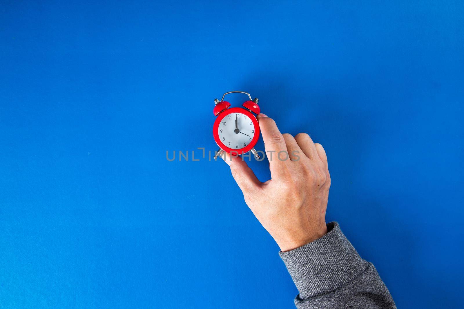 Time optimization concept. hand holding alarm clock on blue background, close up view