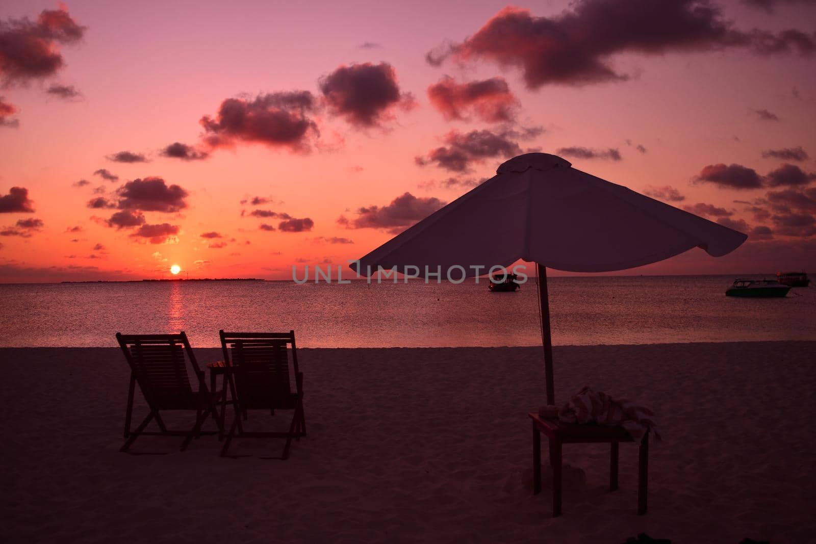 View of umbrella and sunbeds facing the Indian Ocean and the beautiful sunset. by silentstock639