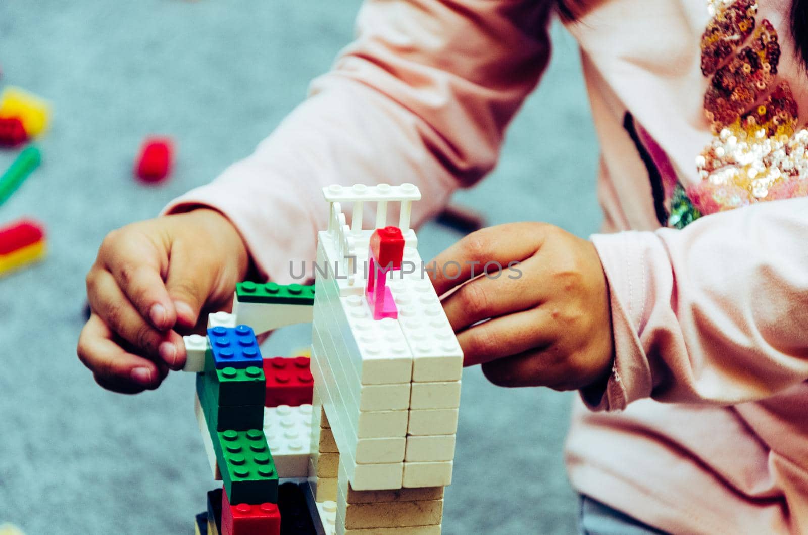 Little girl playing with colorful bricks at home or kindergarten. Closeup