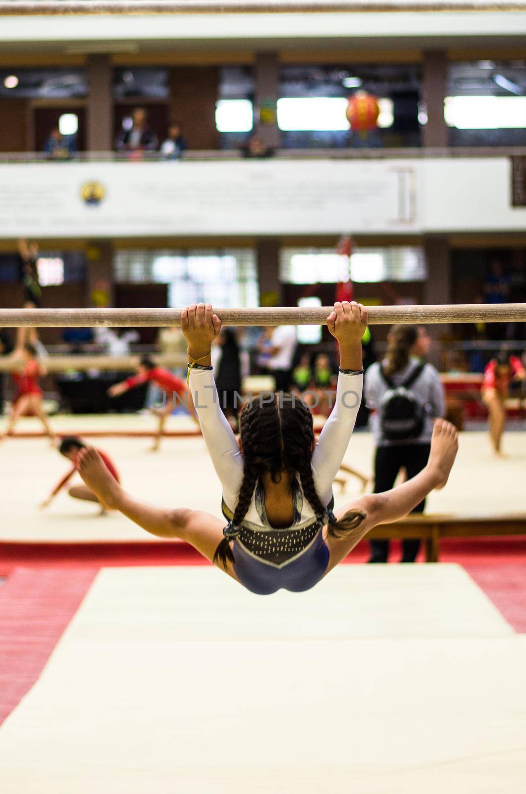 Athletic little girl gymnast performing exercises at the bar in the championship