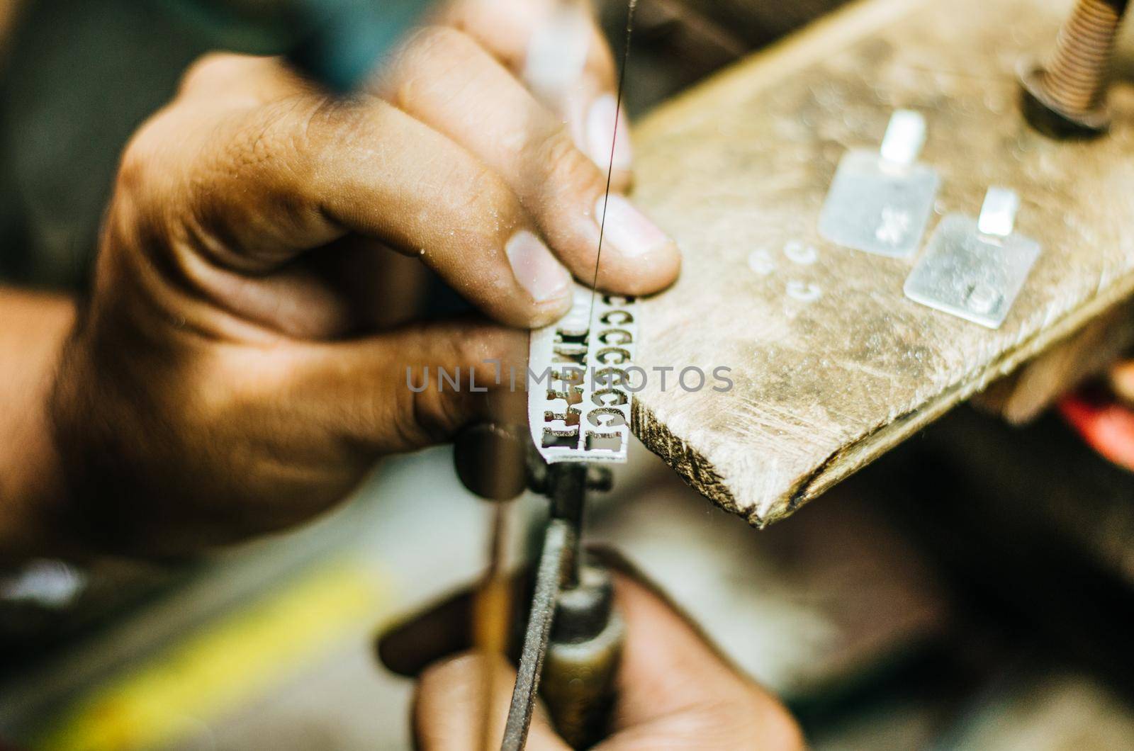 man's hands goldsmith work on a piece of silver with a metal saw on the work table, close up, selected focus, narrow depth of field