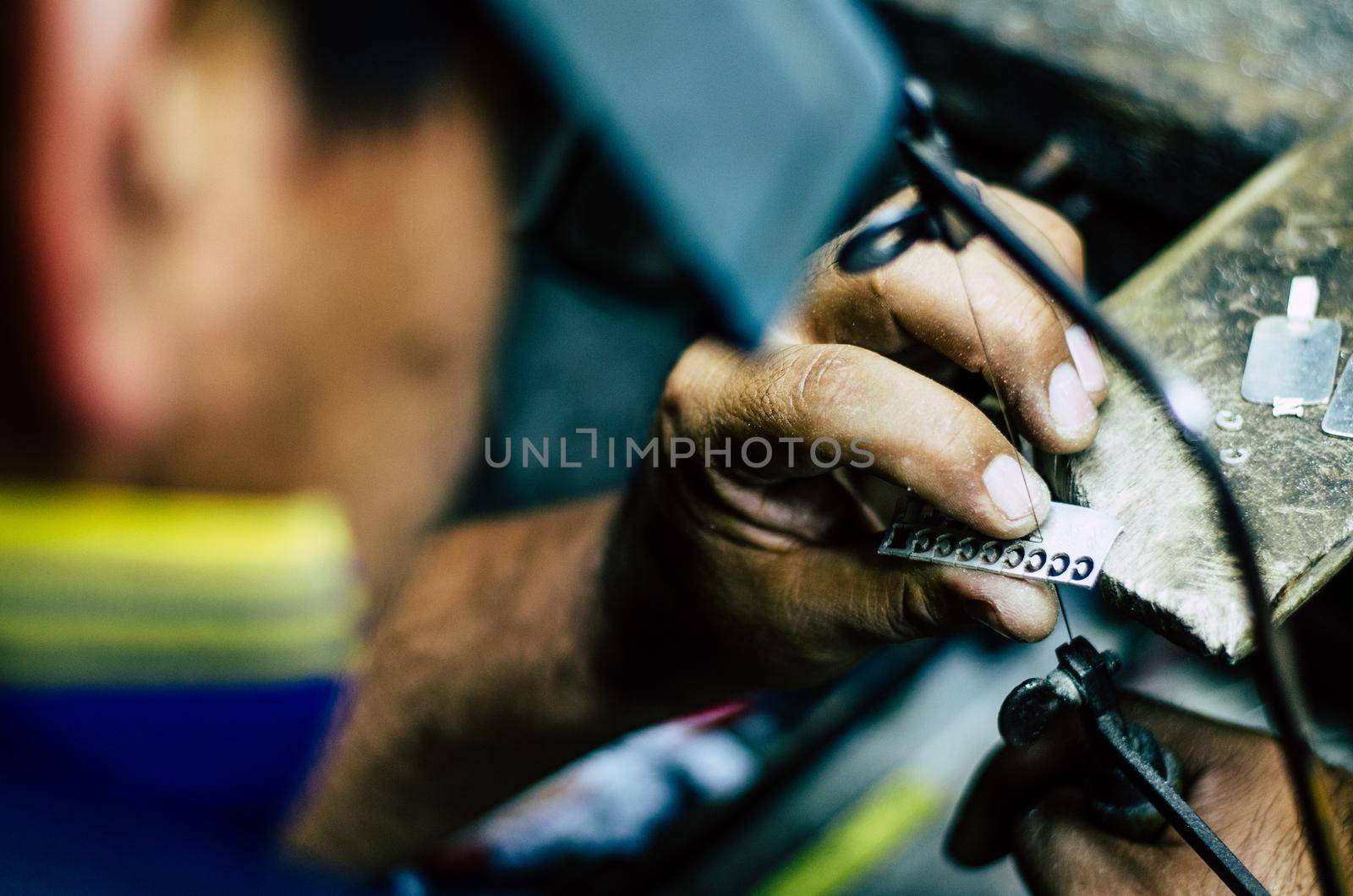 man's hands goldsmith work on a piece of silver with a metal saw on the work table, close up, selected focus, narrow depth of field