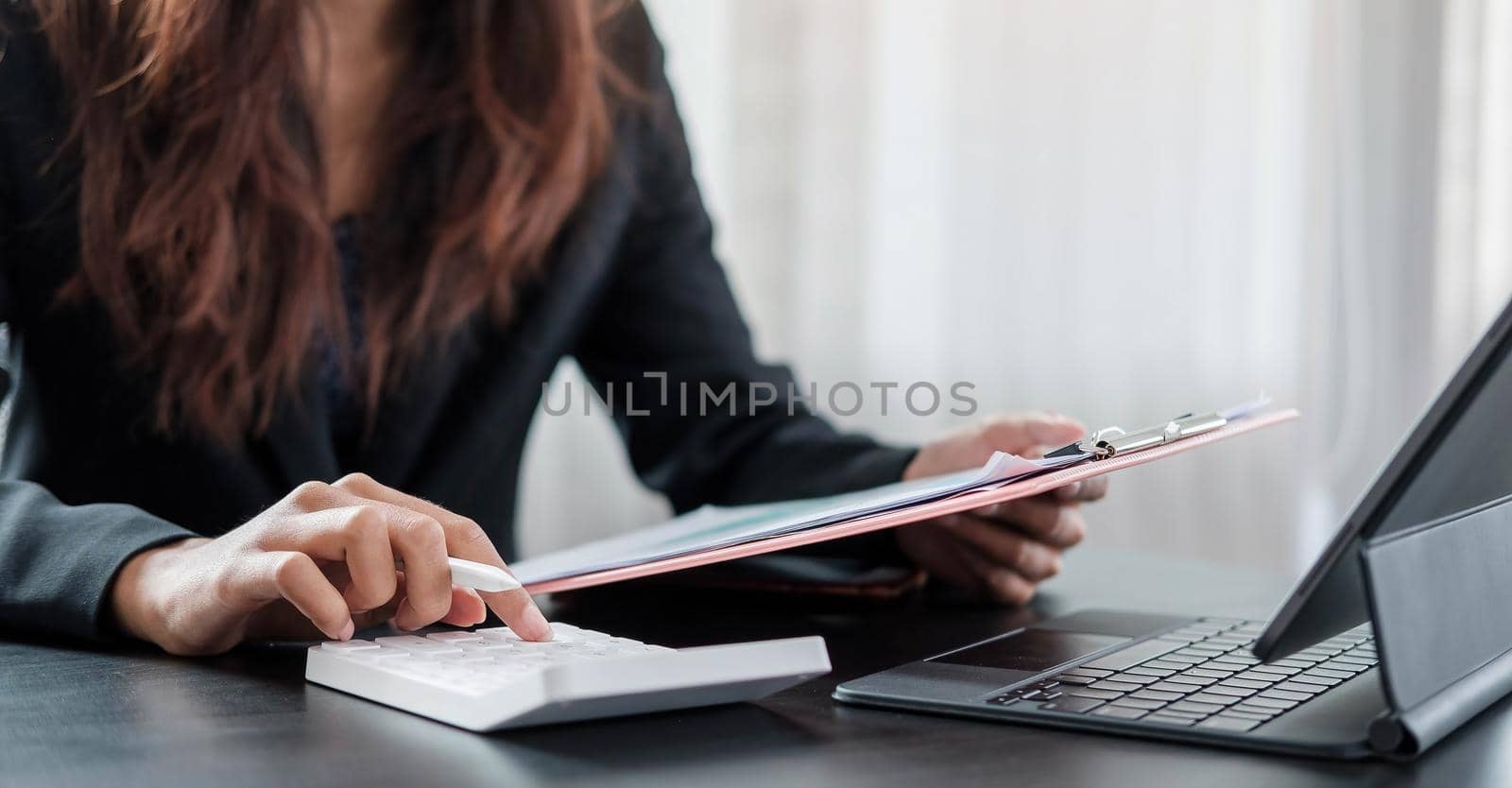 Woman with financial report and calculator. Woman using calculator to calculate report at the table in office by wichayada