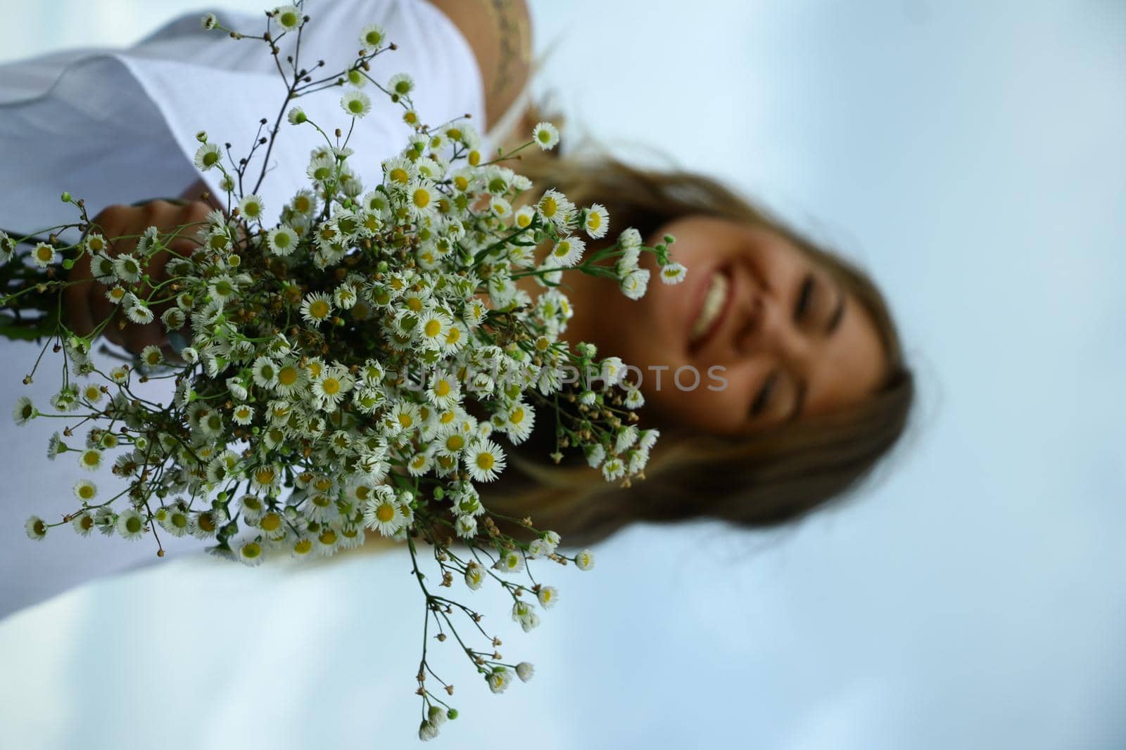 portrait of a happy flirty beautiful blonde woman in white blouse in the field. Carrying a bouquet of daisies. Temporary tattoo. Drawings on body. hippie. Nature loving.