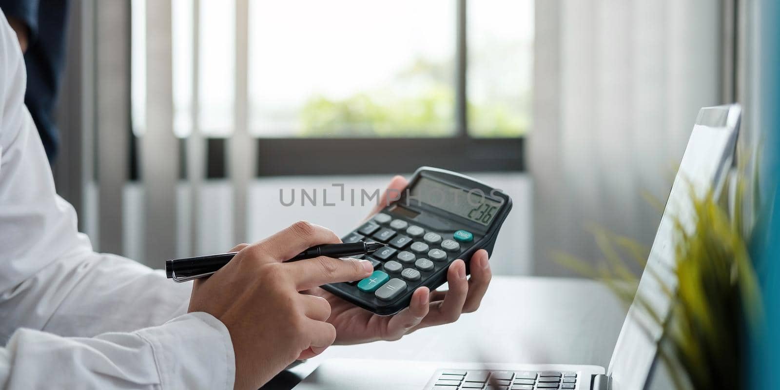 Close up Business woman using calculator and laptop for do math finance on wooden desk in office and business working background, tax, accounting, statistics and analytic research concept.