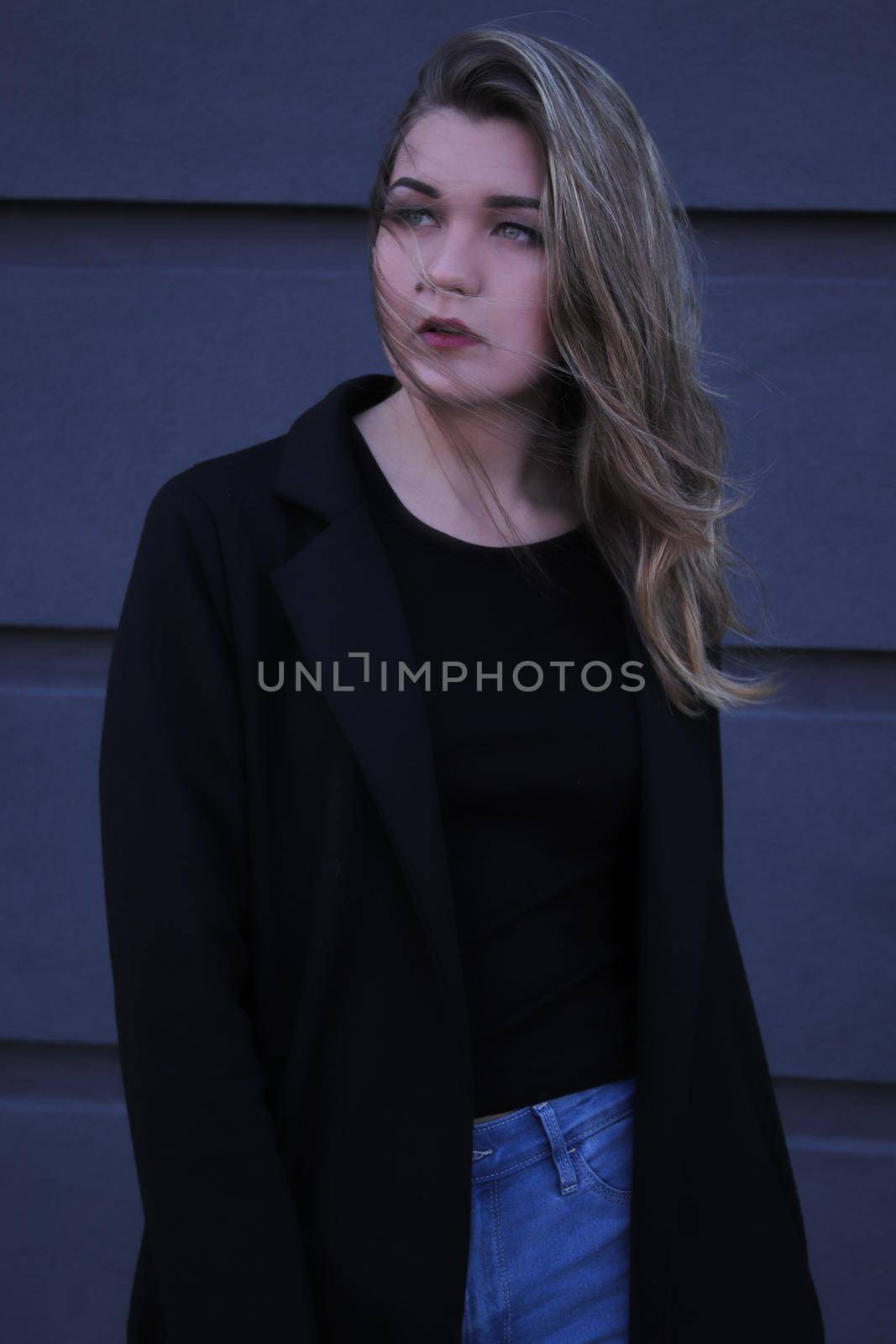 urban portrait of a pensive flirty beautiful woman in black blouse and jeans on a background of gray wall in strips by oliavesna