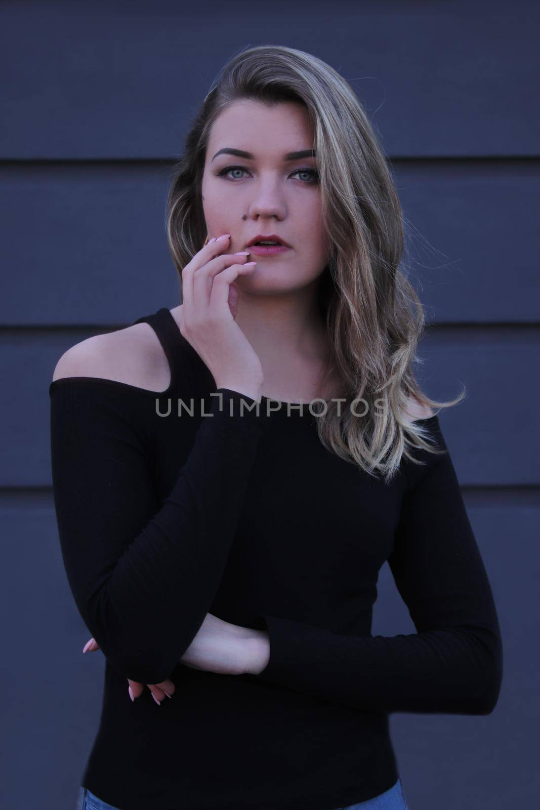 urban portrait of a pensive flirty beautiful young woman in black blouse on a background of gray wall in strips