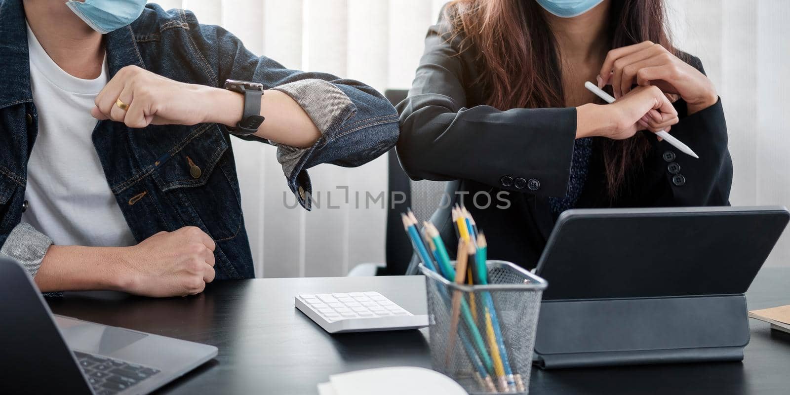 Two young diverse business colleagues wearing face protective masks bumping elbows, greeting each other while working during covid 19 quarantine..
