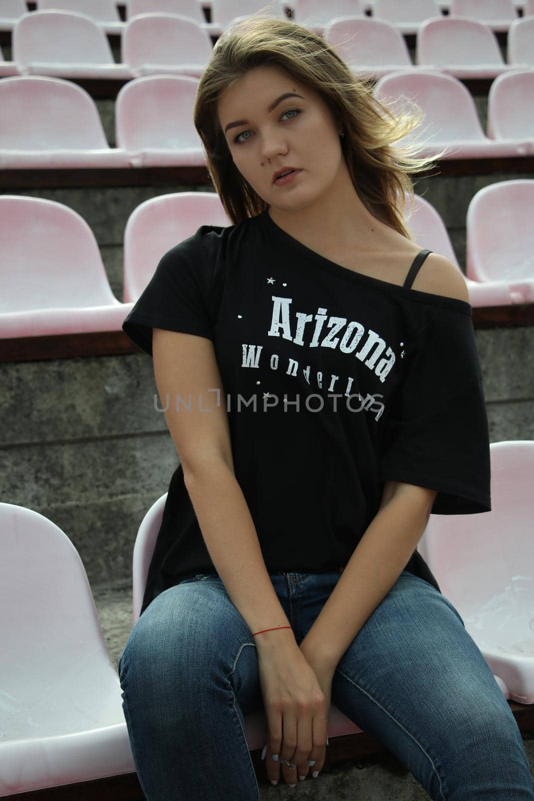 urban portrait of a flirty beautiful woman in black t-shirt and jeans at the stadium, sitting on a bench by oliavesna