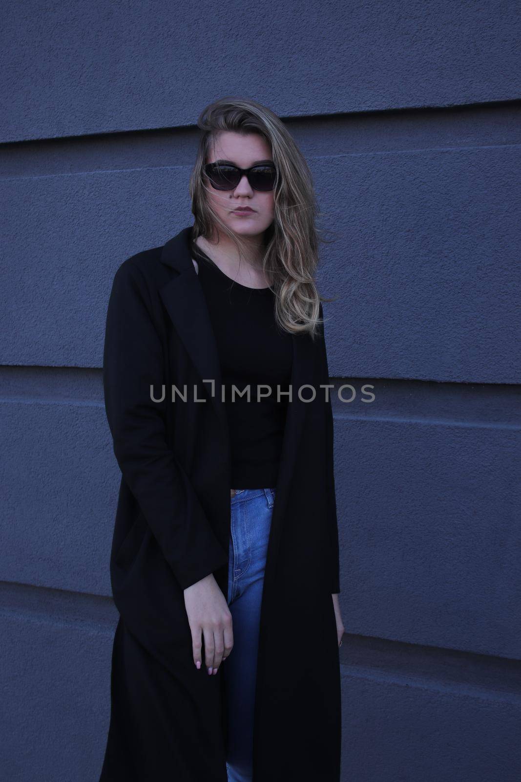 urban portrait of a pensive flirty cool beautiful woman in black blouse and jeans on a background of gray wall in strips