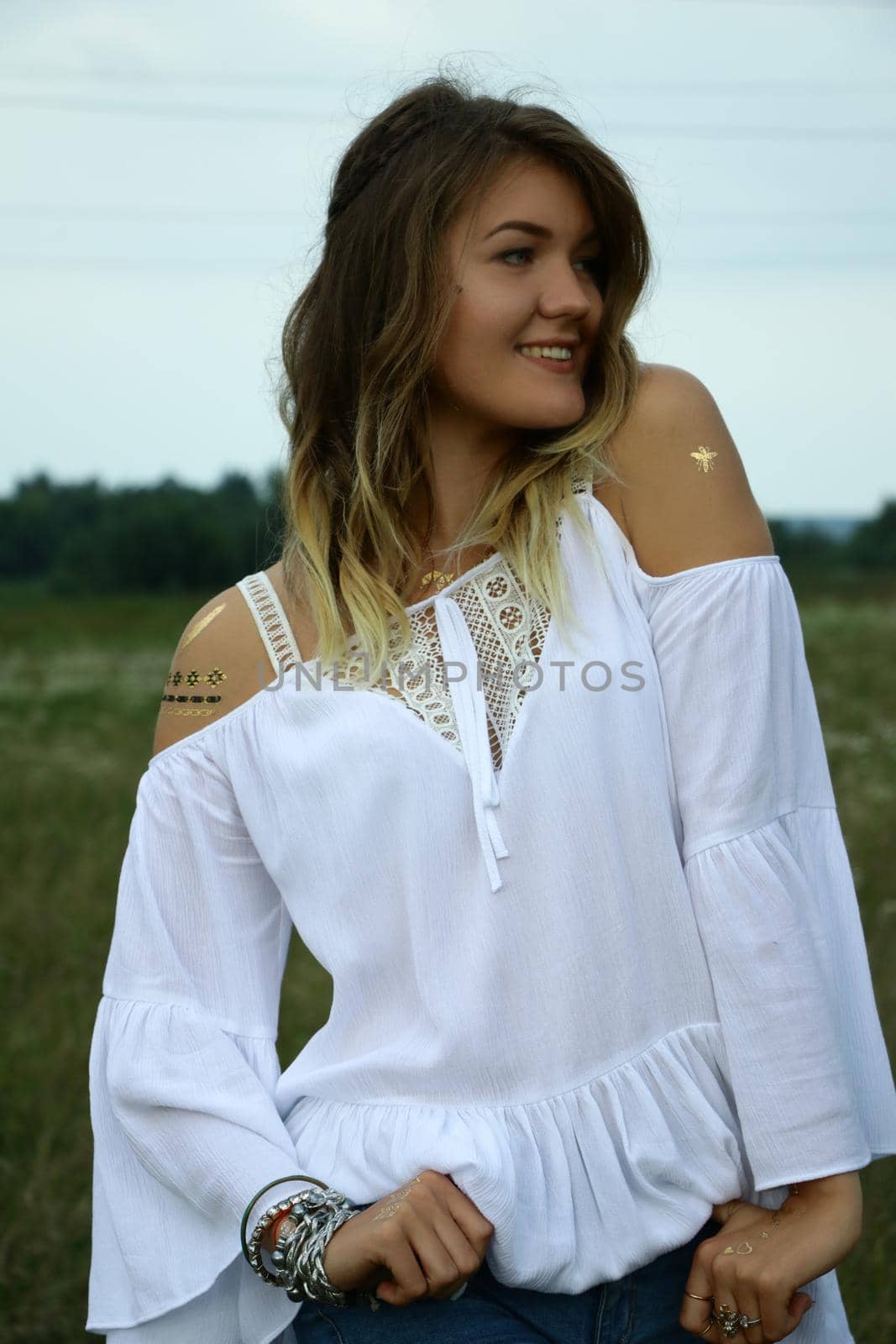 portrait of a happy flirty beautiful blonde woman in white blouse in the field. Temporary tattoo. Drawings on body. hippie. Nature loving.