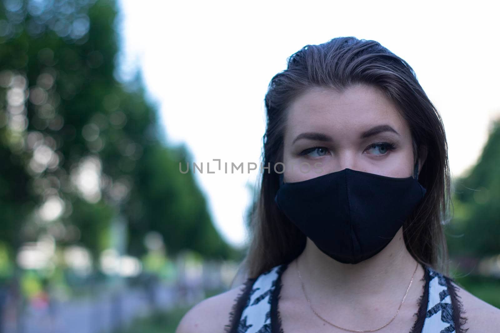 Pretty young blonde woman in medical black face mask. Wearing a t-shirt and jeans shorts. in a park. modern reality. covid-19 concept. copy space. High quality photo