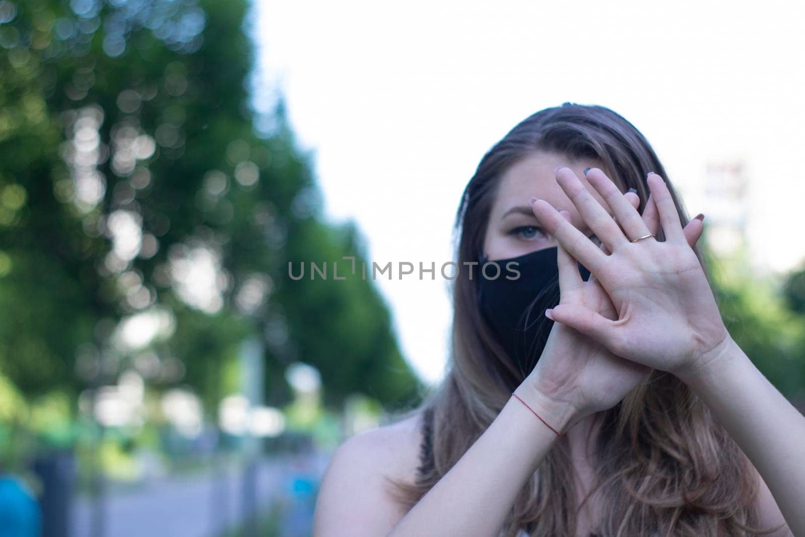 Pretty young blonde woman in medical black face mask. Wearing a t-shirt and jeans shorts. in a park. modern reality. covid-19 concept. copy space. High quality photo