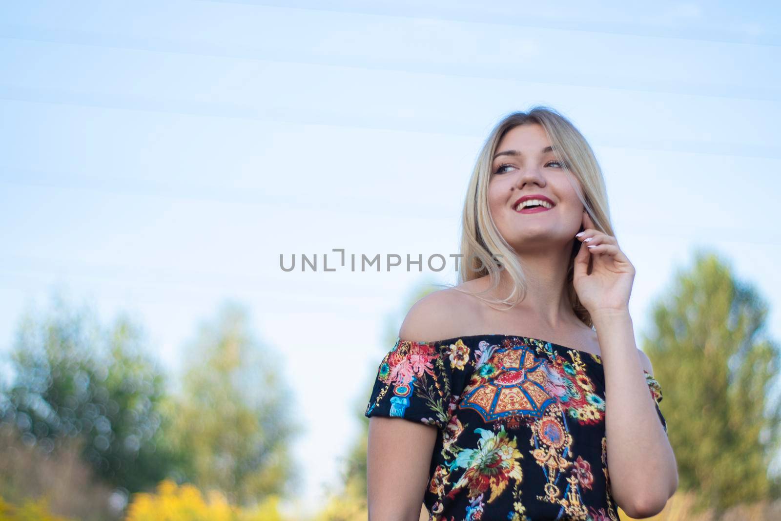 overlight bright portrait of a charming attractive blonde in flowery dress in the field.