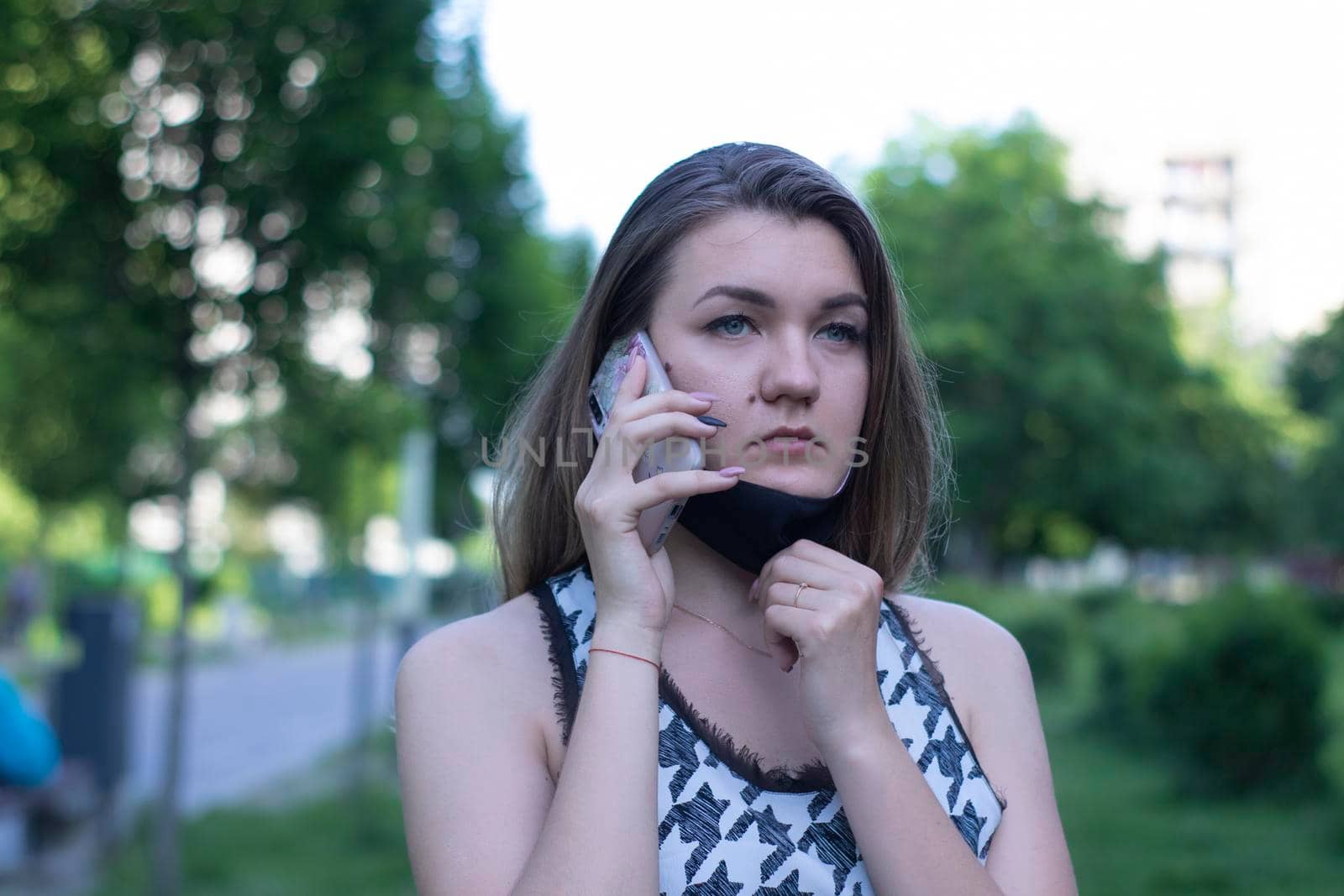 Pretty young blonde woman in medical black face mask. Wearing a t-shirt and jeans shorts. in a park. covid-19 concept. copy space.