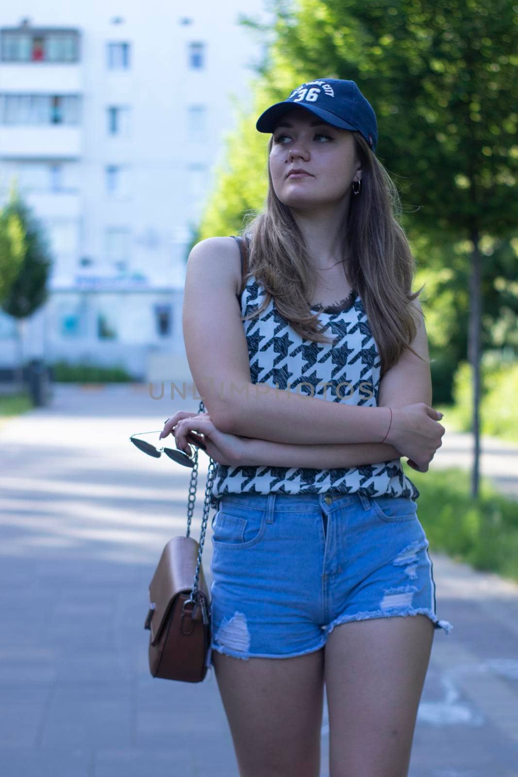 Pretty young blonde woman wearing a t-shirt, jeans shorts and cap. in a park. copy space. High quality photo