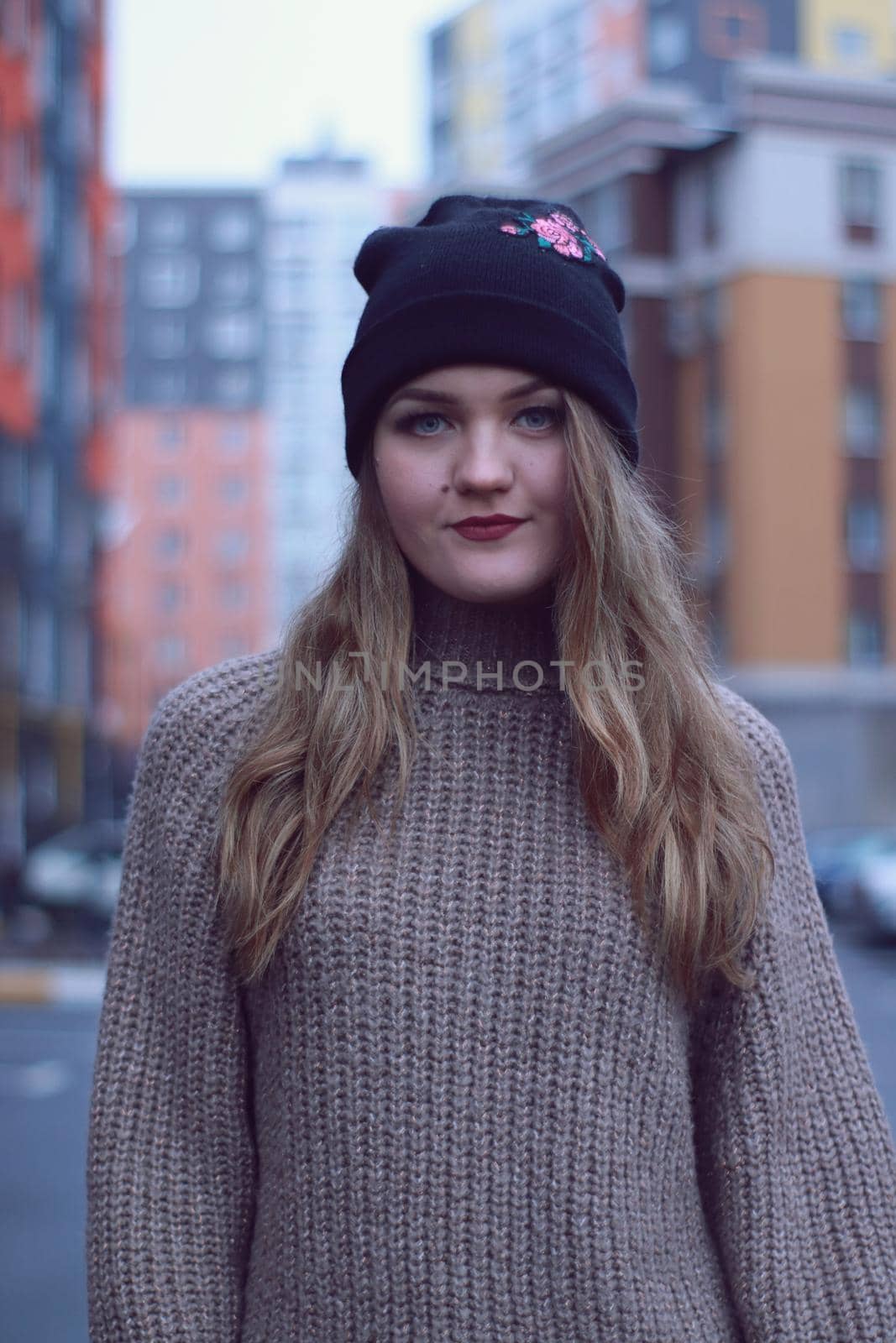 urban portrait of a flirty beautiful woman in knitted brown sweater, jeans and black hat. in the parking lot by oliavesna