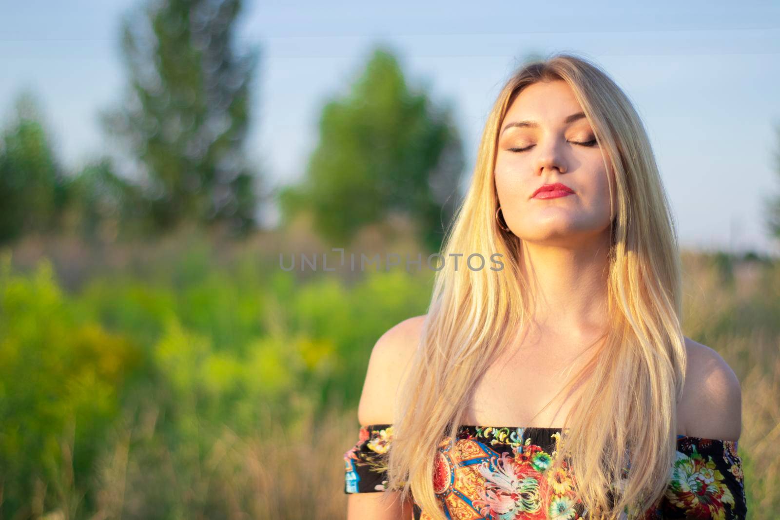 overlight bright portrait of a charming attractive blonde in flowery dress in the field.