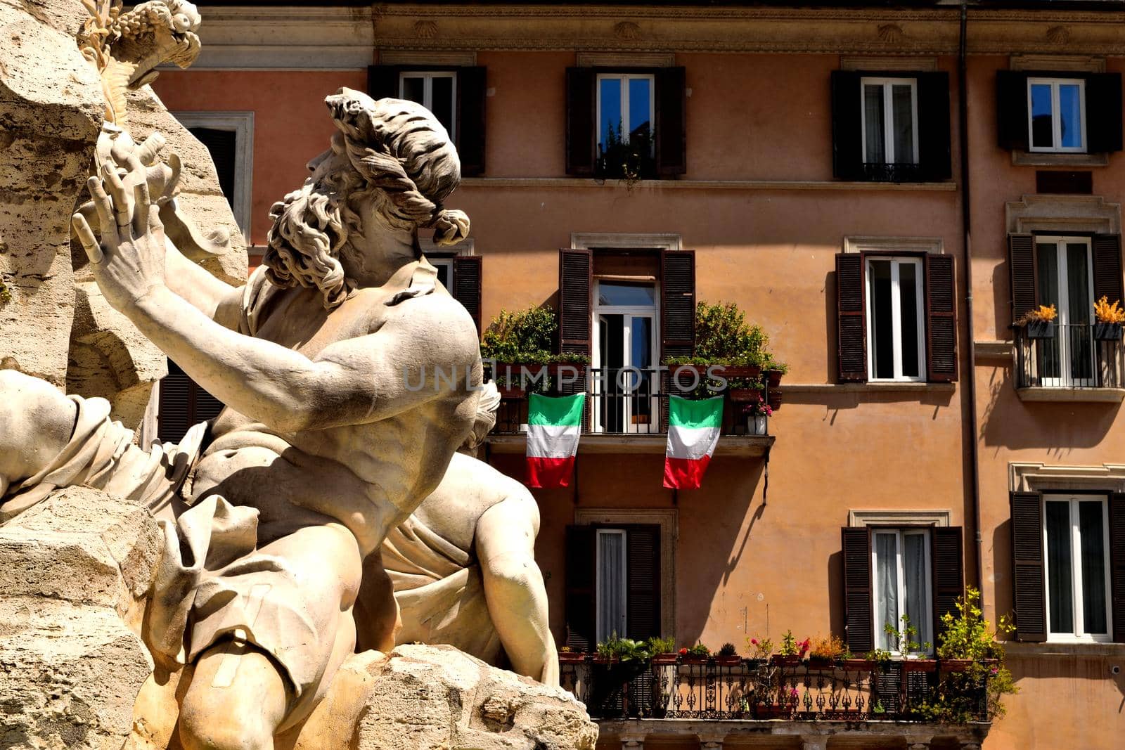 Closeup of the Four Rivers Fountain in Navona Square, Rome, and italian flags during phase 2 of the lockdown by silentstock639