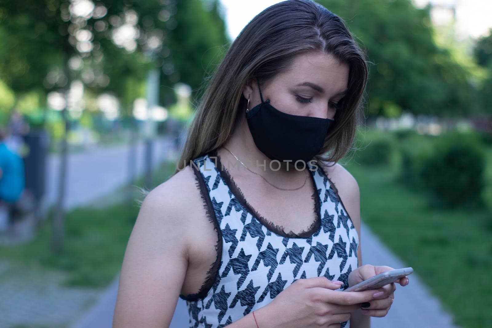 Pretty young blonde woman in medical black face mask. Wearing a t-shirt and jeans shorts. in a park. covid-19 concept. copy space.