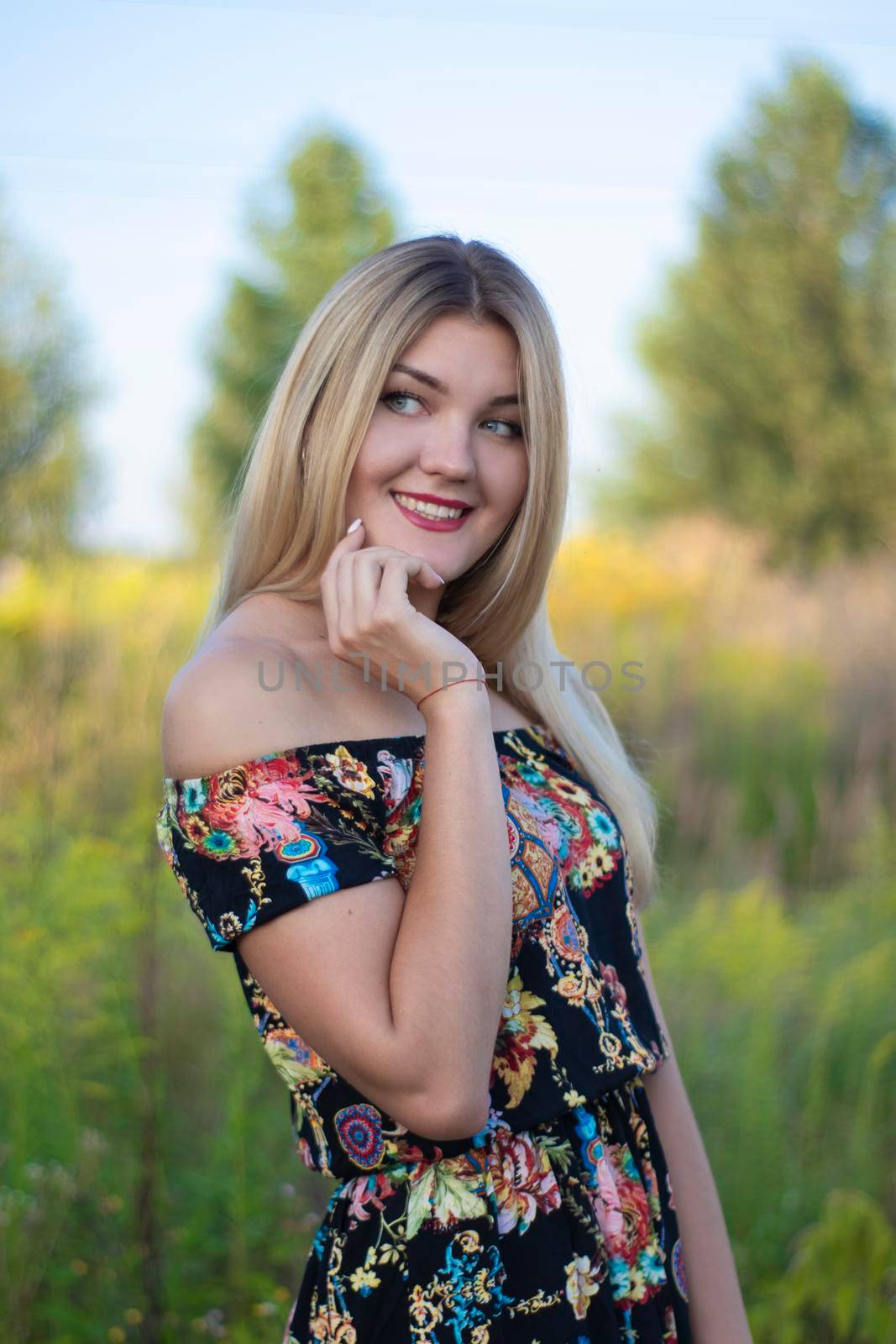 overlight bright portrait of a charming attractive blonde in flowery dress in the field.