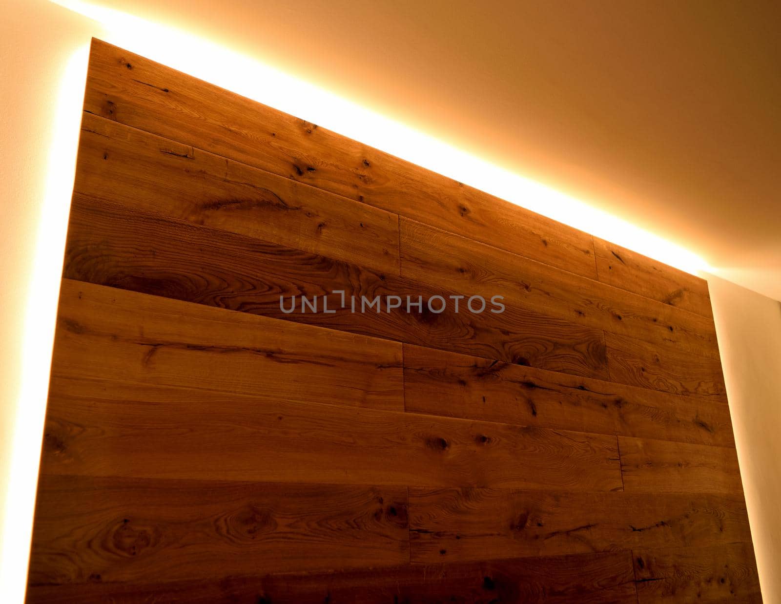 A closeup of a wall covered with parquet with its natural veins, delimited by LED strips.