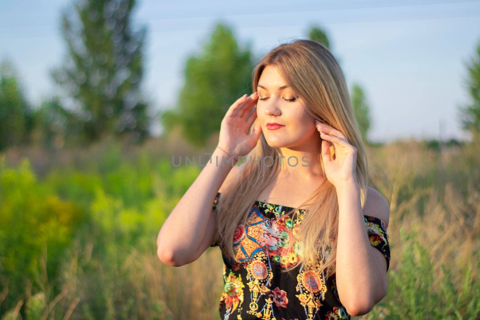 overlight bright portrait of a charming attractive blonde in flowery dress in the field.