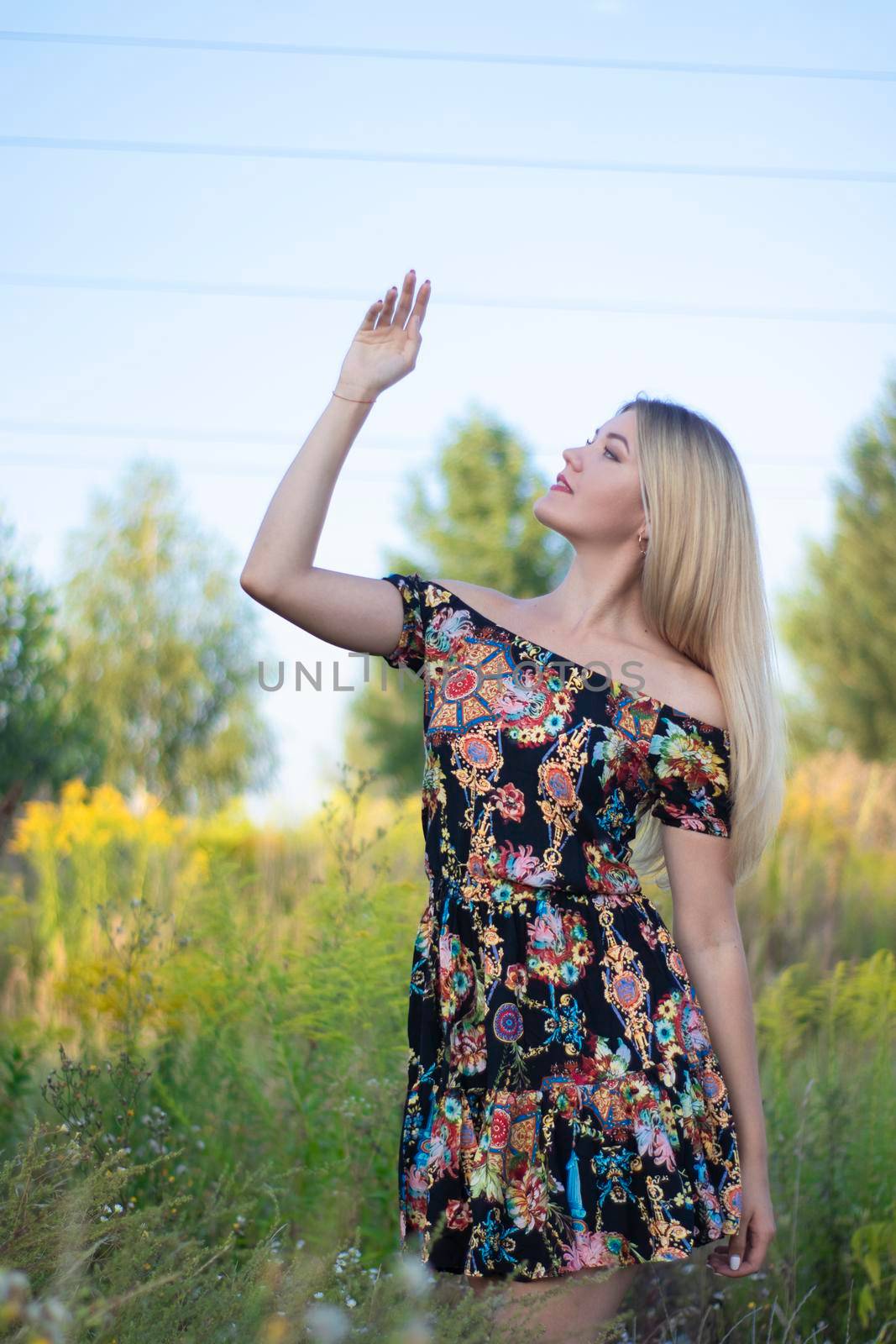 overlight bright portrait of a charming attractive blonde in flowery dress in the field.